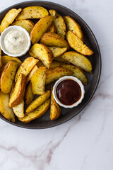 Oven roasted potatoes with skins, sliced, with sauces close-up, top view