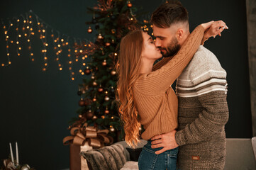 Side view. Standing and embracing each other. Lovely young couple are celebrating New Year at home