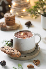 A cup of cocoa with cinnamon and cookies stands on a white table, christmas background, bokeh