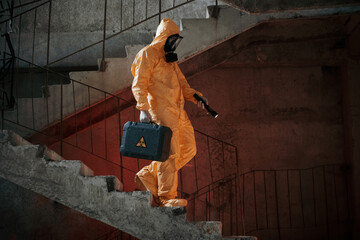 On stairs with flashlight and case. Man dressed in chemical protection suit in the ruins of the post apocalyptic building