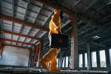Walking with hard case. Man dressed in chemical protection suit in the ruins of the post...