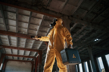 Using the flashlight. Man dressed in chemical protection suit in the ruins of the post apocalyptic...