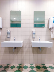 Twin sinks in sanitairy facility with mirrors, soap dispensers and towels. Nice shading pattern created by ceiling lighting. Image taken indoors in Leuven, Belgium.