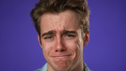 Closeup of sad tired fatigued headache exhausted young man 20s posing isolated on purple background studio. People lifestyle concept. Put hands on head