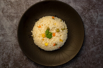 bowl with delicious rice and vegetables on black background, top view