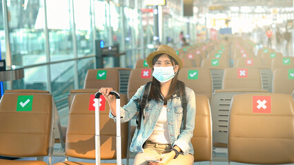 Asian woman traveler wear protective mask sitting with distance at the airport.