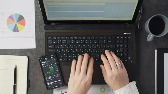 Close-up of a man's hands working on a laptop in the office. Businessman typing text and looking at phone at workplace. High quality 4k footage