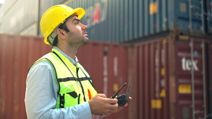 Logistic staff flying drone to survey and inspect stack container in shipment company area.