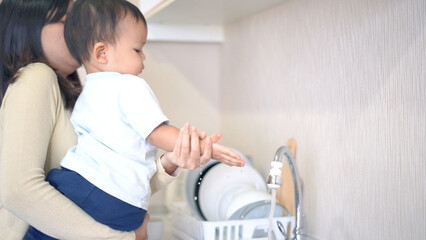 Mother and little boy washing hands in kitchen to keep cleaning.