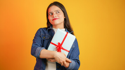 Portrait of an attractive cheerful happy girl holding gift box in hand, Young Asian Indian woman with gifts isolated over color background