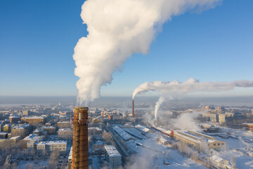 Brick factory chimney with white smoke on the background of a winter cityscape. Aerial view.