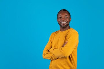 Cheerful confident black man smiling over blue background, copy space