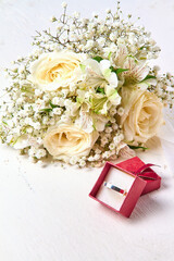 Silver ring in red gift box and bouquet of flowers on white textured wooden background, holiday