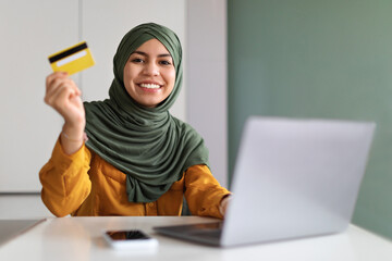 E-Commerce Concept. Smiling Muslim Lady Holding Creadit Card And Using Laptop