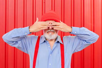 an elderly man covering his eyes with his hands on red background