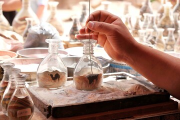 Close up of hand with filament, which is making camel in bottle with colorful sand. Petra, Jordan