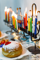 Hanukkah menorah, candelabra, with candles and sufganiyah doughnut.