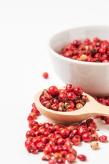 Fragrant spice pink pepper seeds in wooden spoon and a small white ceramic bowl. Close up pink peppercorn isolated