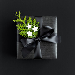 Black gift box with a black ribbon, thuja and stars on a dark background. Top view.