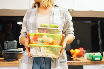 Hands of woman hold plastic containers with different frozen foodstuffs. Hermetically sealed food storage. Cooking.