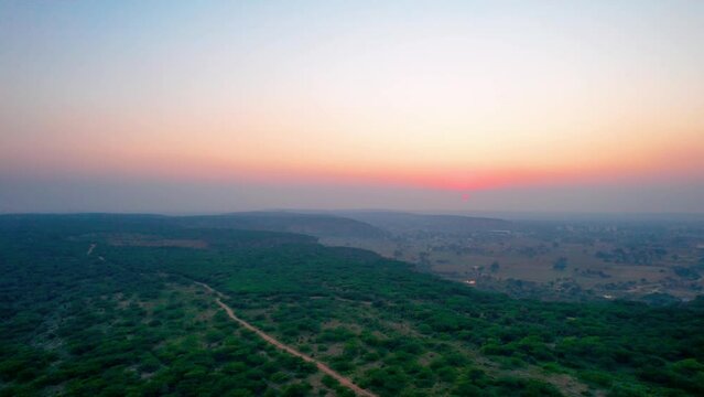 aerial drone panning shot showing sunset dusk colors over tree covered mountain top with small dust trail and fog covered mountains in the distance shot at leopard trail gurgaon haryana popular local
