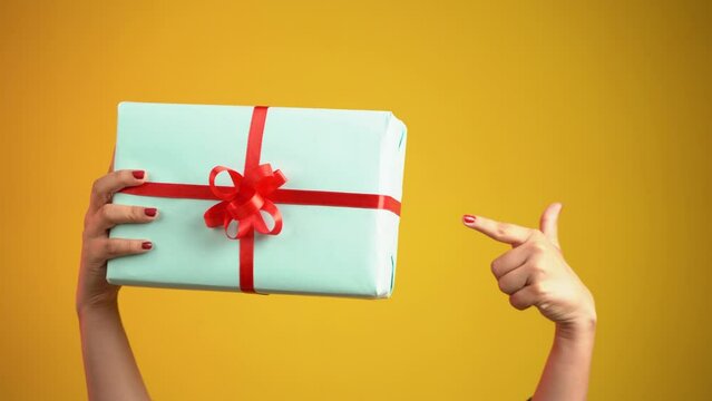 Close up of a female hand holding gift box, isolated over orange color background