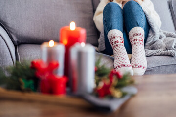 Obraz na płótnie Canvas Female feet in xmas woolen socks and cozy Christmas mood candles composition for hygge home on the coffee table. Interior and home coziness concept. Winter and Christmas holidays. Selective focus.
