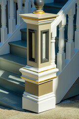 White and beige colored hand rail banister with classic american style and stairs in shade with sun early morning on porch