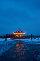 Carousel roundabout, galloper at the center an amusement park in the evening at night illumination. Outdoor vintage colorful luminous. Winter time, snow. Blue background. Copy space, vertical photo