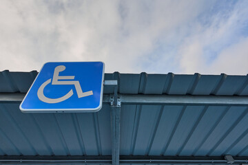 Obraz premium Free parking space reserved for the handicapped with the international handicap symbol painted in white on bright blue on a plaque on the top of the roof of the reserved space under the cloudy sky.