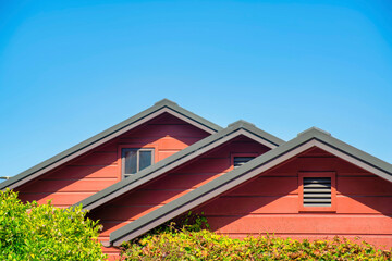 Row of double gable style roofs with red stucco exterior and dark accent paint around edges with visible insulation vents