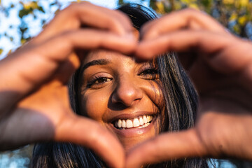 Frontal view of happy woman laughing at camera and making a heart shape with hands .