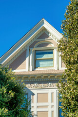 Wooden house facade with beige exterior and white accent beams and paint with front yard trees and clear blue sky