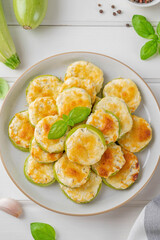 Baked zucchini with cheese, garlic and fresh herbs on a white wooden background. Selective focus