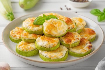 Baked zucchini with cheese, garlic and fresh herbs on a white wooden background. Selective focus
