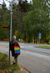 Unrecognised woman with colourful hand bag waiting on the bus stop. People travelling. Public transportation