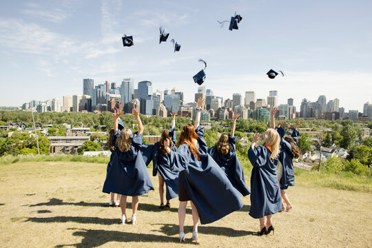 High School Girl Graduates Throwing Mortarboards In Sunny City Park