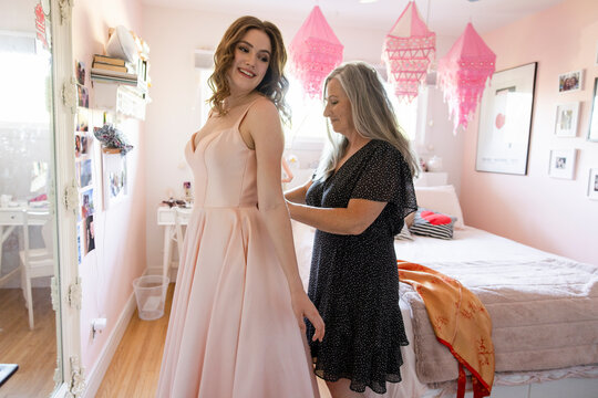 Mother Helping Daughter With Pink Prom Dress In Bedroom