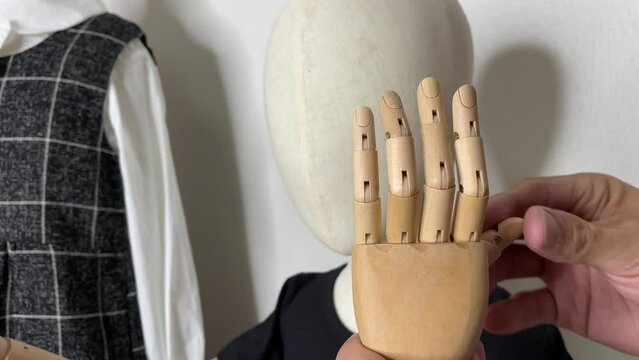 Male hand adjusting child mannequin wooden fingers showing "I love you" hand gesture 