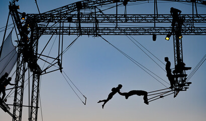 silhouettes of trapeze artists acrobats on the metal scaffolding at sunset