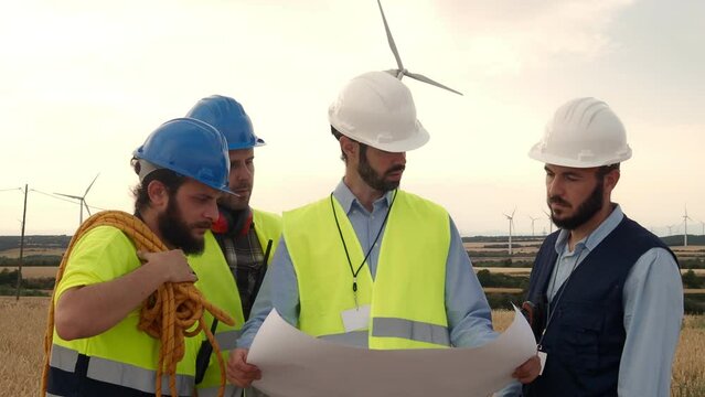 Group of Caucasian male engineers looking at a blueprint in a windmill park 
