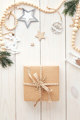 Handcraft paper gift box with nordic Christmas decoration and fir branches on white wooden table. Top view, overhead.