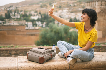 Young brunette woman doing a selfie in La Alhambra, Granada with her smartphone