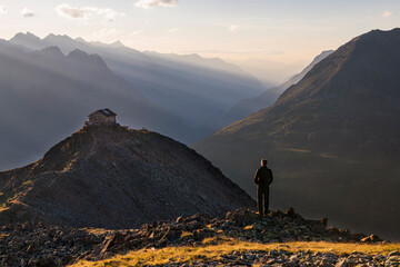 Ein Wanderer beobachtet den Sonnenuntergang über dem Gipfeln bei Sölden vor der Brunnenkogelhaus...