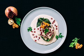 Top view of gourmet dish on black background, chile en nogada with pomegranate, cilantro and walnut.