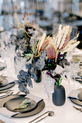 Close up of banquet setting with ceramic vases of flowers and dark plates during celebration event