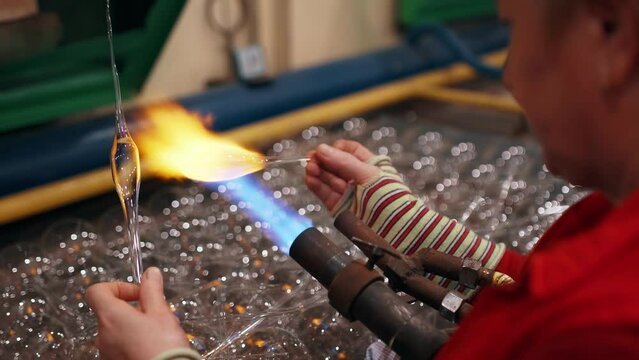 Side view of a female worker who heats a glass to blow a Christmas toy.