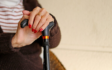 The painted nails of an older woman's hands, holding a cane
