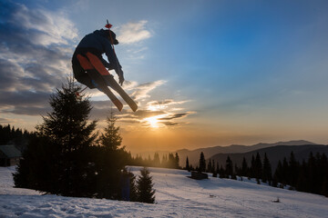 Freestyle extreme skier jumping from kicker in snowy mountains at orange sunset - obrazy, fototapety, plakaty