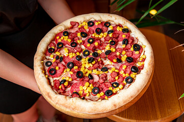 Tasty and big pizza with different types of meat. Pizza with sausage, ham, corn and olives.